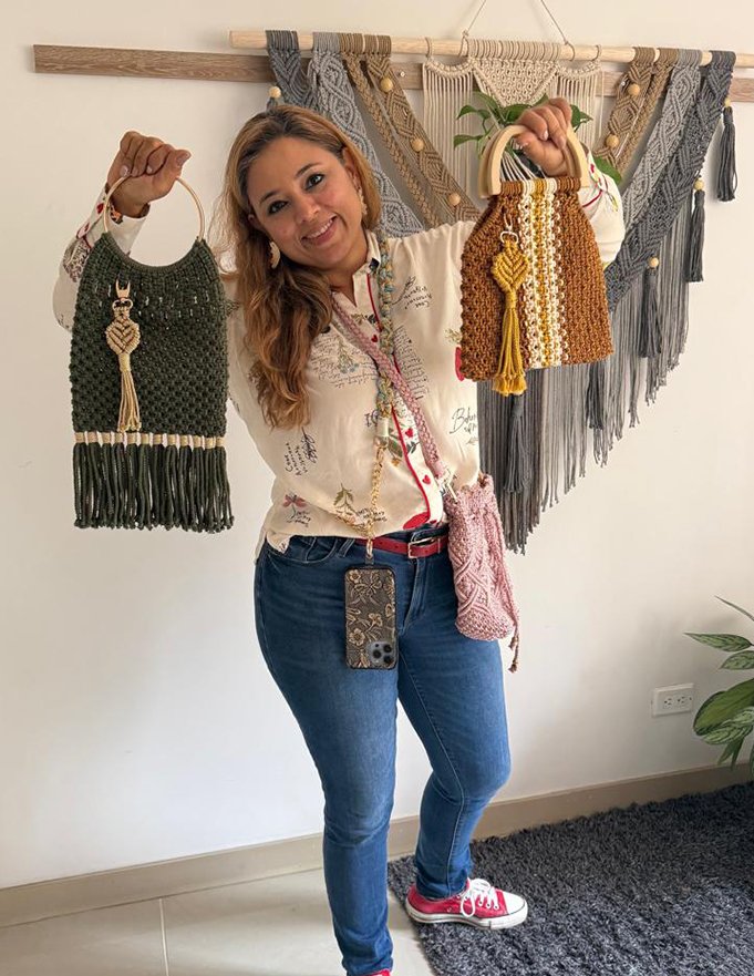 Estudiante mostrando sus bolsos de macramé frente a un tejido de pared